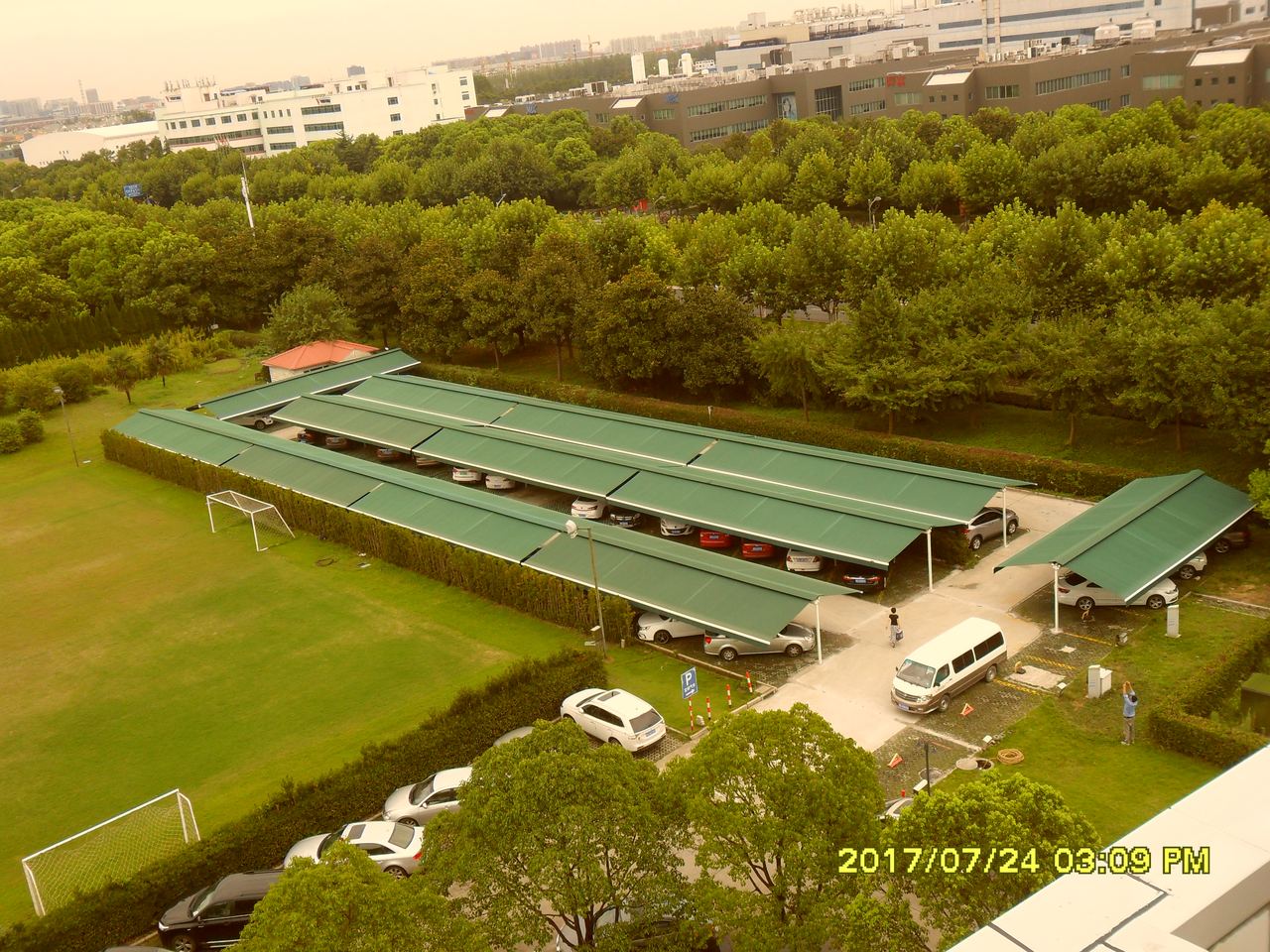 上海宝钢气体有限公司停车场遮阳篷项目完工实景:宝信软件园内成排绿色伸缩臂遮阳篷覆盖停车场,与周边绿化、道路成片布置