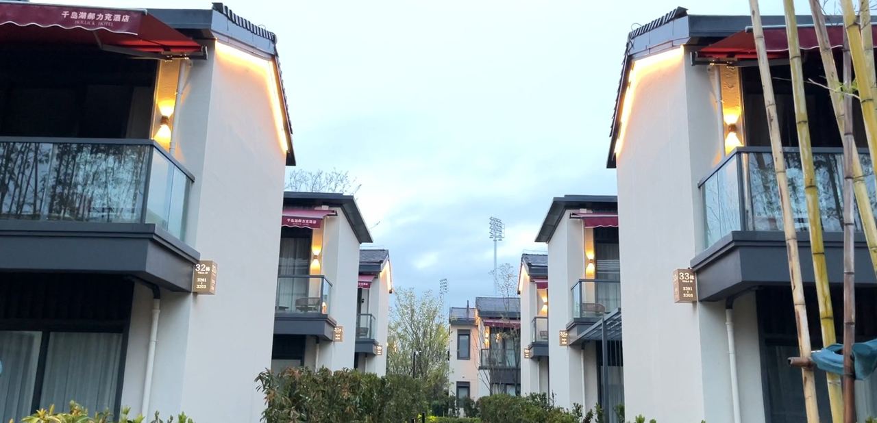 2022杭州亚运度假村2-12地块别墅客房区室外雨棚实景:千岛湖郝力克酒店(HOLLY&K HOTEL,业主中国绿发)2-12 地块内成排独栋别墅,每栋客房二层阳台外沿均设红色伸缩雨棚,通道两侧 32、33 幢雨棚成片布置